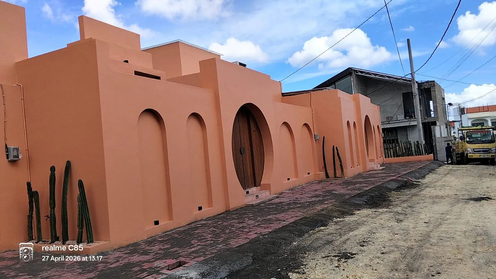 Canggu Villa on site — terracotta perimeter wall with arched openings and a carved timber pivot door, April 2026