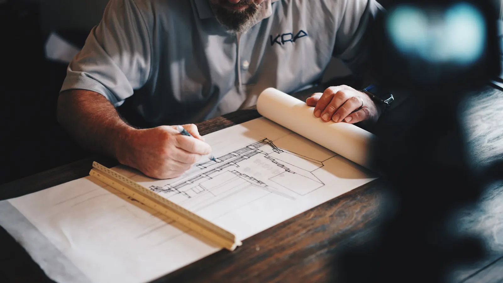 Architect sketching a building elevation by hand, with a ruler and rolled drawings on the desk
